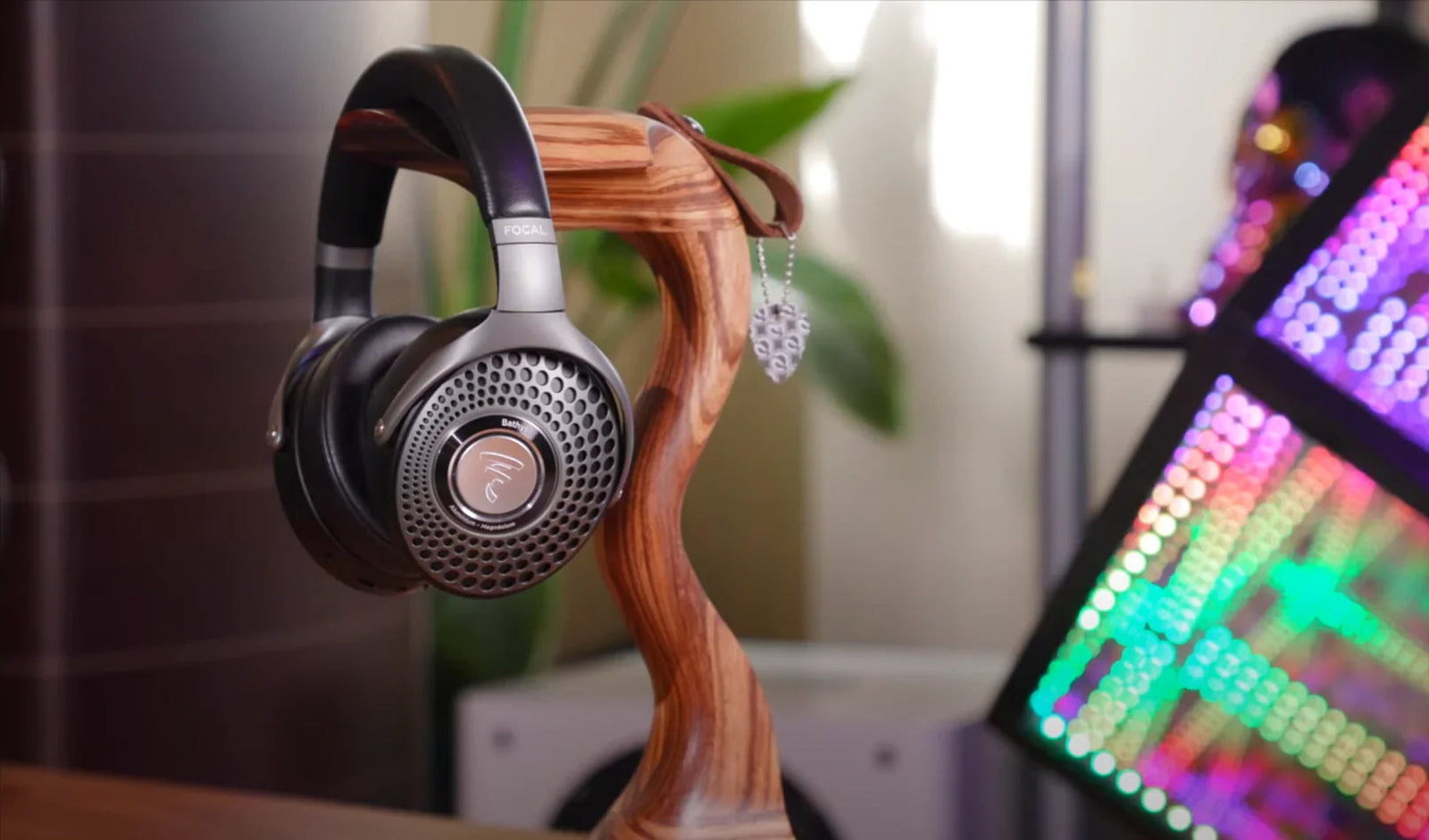 Focal Bathys wireless Bluetooth HiFi headphones on a wooden stand, with colorful LED lights and decor in the background at The Source AV.