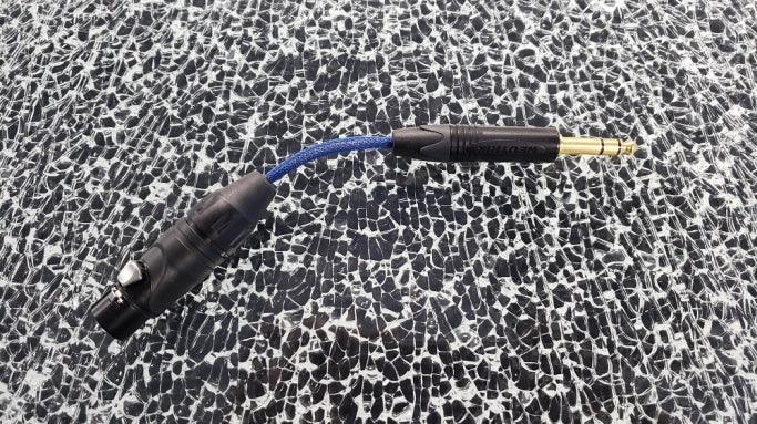 XLR to 1/4 inch audio adapter cable with blue braided cord on a textured glass surface
